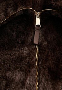 Primo piano di un tessuto morbido di colore marrone scuro con una cerniera dorata e un tirante in tessuto parzialmente chiuso.