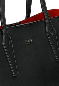 Černá kožená taška přes rameno s dvojitými ušima, červeným interiérem, vyraženým logem a kontrastními švy. Hladká textura, obdélníkový tvar.