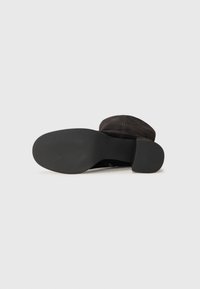 Bottine en suède noir avec un bout rond, une tige lisse et une semelle en caoutchouc texturée. Caracterisée par un petit talon empilé.