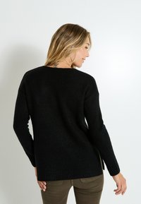 Suéter de punto negro con mangas largas, escote redondo y dobladillo acanalado. Presenta un corte holgado y aberturas en los laterales para facilitar el movimiento.