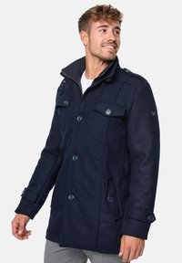Navy blue wool-blend coat with double-breasted buttons, epaulets, and side pockets; features a high collar and a smooth texture.