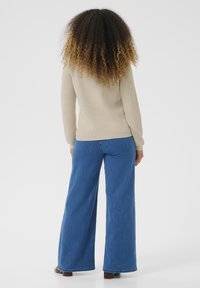 Beige ribbed sweater paired with wide-leg blue jeans, featuring a smooth texture and relaxed fit, seen from the back against a plain background.