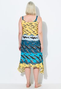 Vestido sin mangas con una parte superior amarilla vibrante decorada con patrones de peces, que pasa a un tono azul con gráficos de tiburones, terminando en un dobladillo asimétrico.