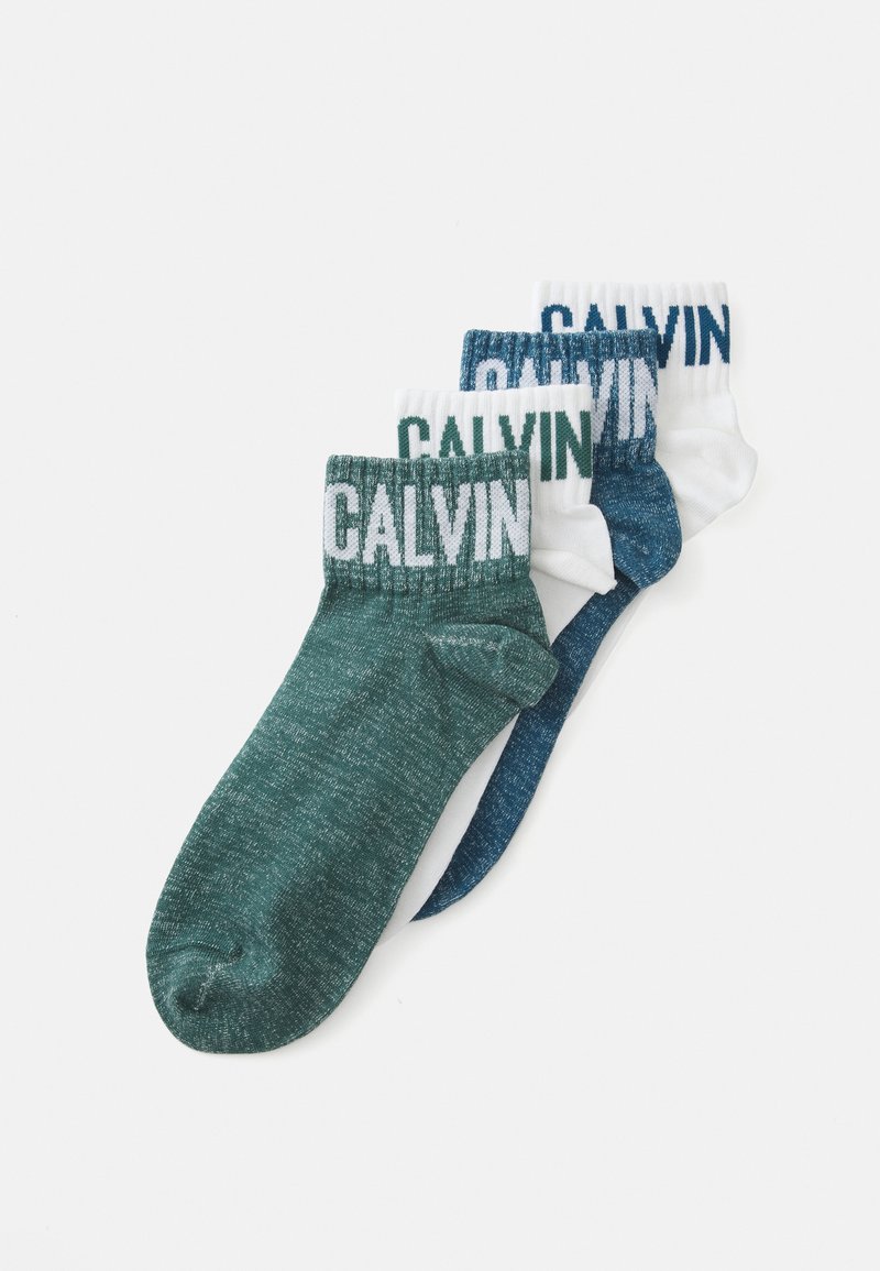 Três pares de meias de tornozelo: verde escuro, azul-marinho e brancas; cada uma com um logo "CALVIN" em contraste na parte superior. Textura de malha suave.
