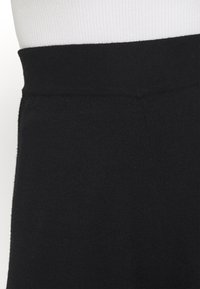 Black waistband made of soft, stretchy fabric. Smooth texture with a seamless finish, tapering into a fitted silhouette.