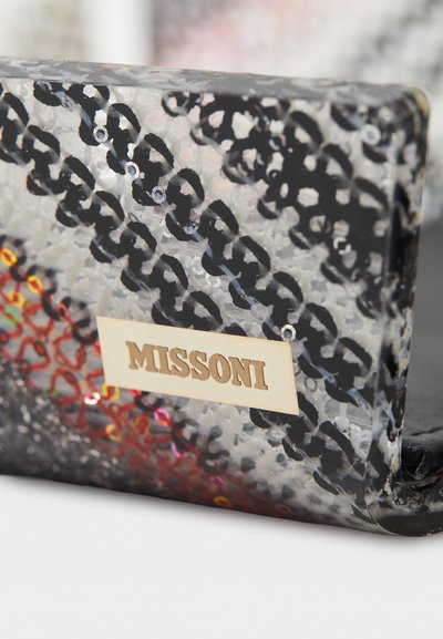 Pochette en plastique translucide noir et transparent avec un motif en chaîne, des accents rouges et une étiquette logo Missoni visible sur un côté.