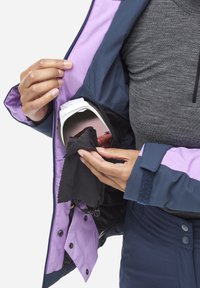 Veste imperméable aux couleurs marine et lavande, dotée d'une poche interne contenant un chiffon de nettoyage et un objet rond.