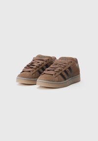 Brown suede low-top sneakers with three black stripes, round toe, flat rubber sole, and padded collar. Features lace-up design.