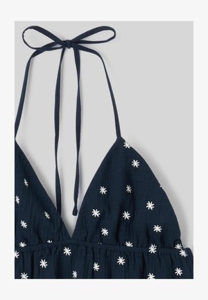 Haut dos nu bleu marine avec des motifs d'étoiles blanches brodées et une lanière nouée autour du cou sur un fond clair uni.