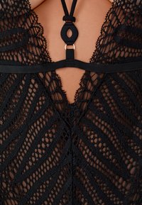 Close-up van zwarte kanten lingerie met geometrische patronen en een band met een kleine decoratieve ring in het midden.