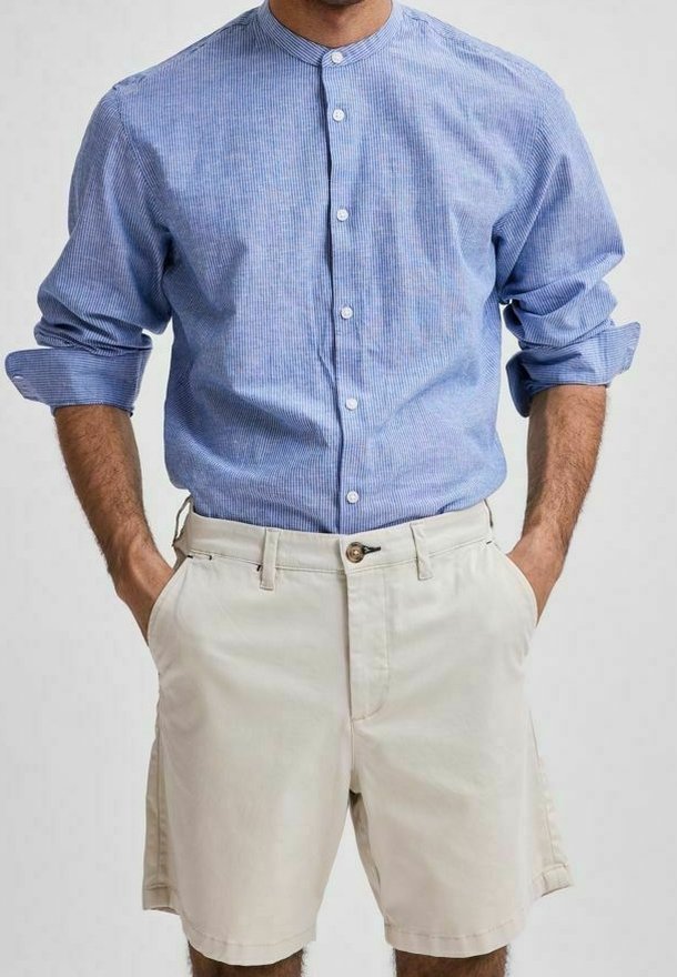 Camicia azzurra a righe con colletto alla mandarino, abbinata a pantaloni corti beige con chiusura a bottone singolo e tasche laterali.