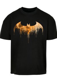 Melna kokvilnas T-krekls ar lielu, pilējošu zelta un oranžu Betmena emblēmu centrā. Īsas piedurknes un apaļa kakla izgriezums.