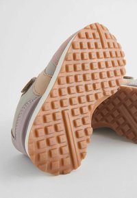 Semelle de sneaker légère avec une adhérence en caoutchouc texturé corail. La tige présente des panneaux beiges, gris et roses ; comprend une sangle Velcro.
