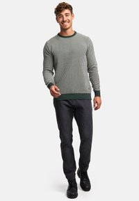 Grå og grønstribet sweater med lange ærmer og ribbede manchetter, parret med mørke jeans og sorte støvler, der har rund halsudskæring.