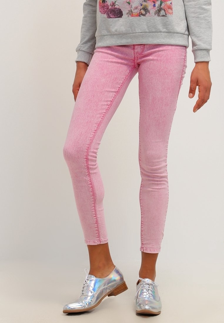 Henkilö, jolla on päällä vaaleanpunaiset skinny-farkut, harmaa kukkakuviollinen collegepaita ja kiiltävät hopeiset nauhalliset kengät matalilla puukoroilla.