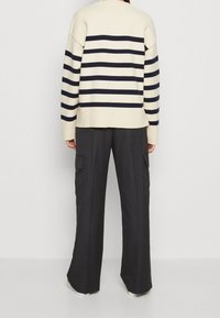 Gestreepte trui in crèmekleur en marineblauw, met geribbelde manchetten en een rugsplit, gecombineerd met donkere, wijde cargo-broek met zijzakken.