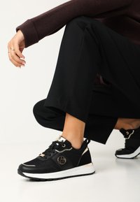 Czarne sportowe sneakersy z teksturowaną siateczką, złotymi akcentami, białą podeszwą środkową i logo. Zaprojektowane z sznurówkami i zaokrąglonym czubkiem.