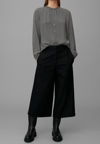 Svart och vit mönstrad blus med långa ärmar, knappstängning fram, och draperad halsringning, ihop med svarta vida byxor och svarta stövlar.