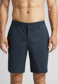 Námořnické modré šortky vyrobené z hladkého materiálu, s knoflíkovým zapínáním, bočními kapsami a rovný střih, který končí nad kolenem.