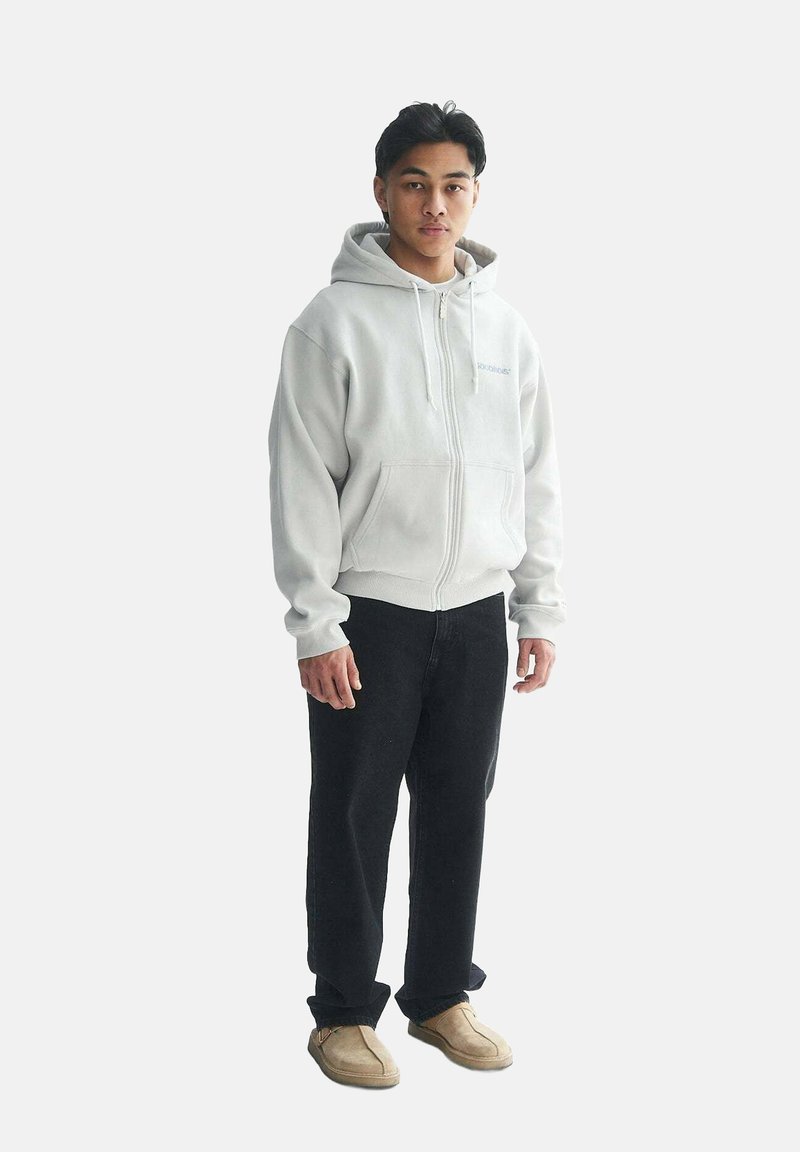Light gray zip-up hoodie with a front pocket, worn with black pants and beige shoes. Smooth fleece texture, casual fit, no visible patterns.
