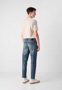 Tricou scurt bej deschis, purtat cu blugi decolorati blue, având o croială relaxată și un look casual. Adidașii albi completează ținuta.