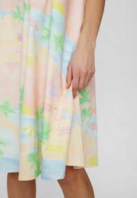 Robe imprimée plage colorée avec des tons pastel, des palmiers, des parasols et un flamant rose, en tissu léger à la texture lisse.