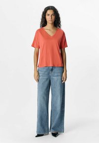 Koralfarvet V-hals t-shirt med løse korte ærmer, kombineret med højtsiddende, bredbenede lyseblå jeans og sorte spidse sko.