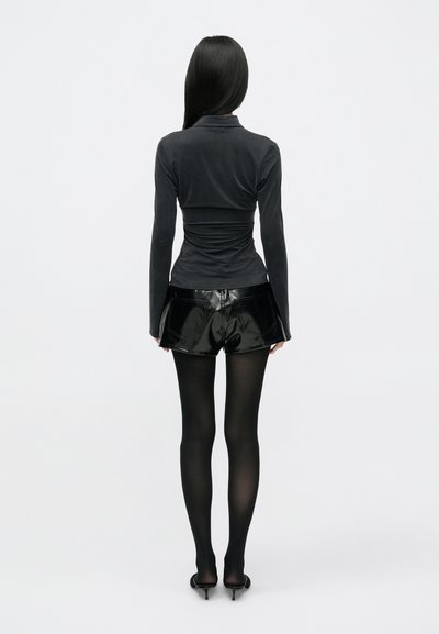 Black long-sleeve, form-fitting top, paired with shiny black shorts. The model wears black tights and heels. Smooth textures and fitted design.