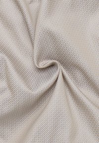 Tessuto testurizzato in beige chiaro con un motivo geometrico. Materiale morbido con una leggera lucentezza, che evidenzia un aspetto drappeggiato.