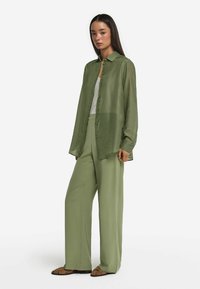 Genomskinlig grön skjorta, knäppning framtill, kombinerad med matchande vida byxor och bruna platta sandaler. Minimalistisk look med mjuka texturer.