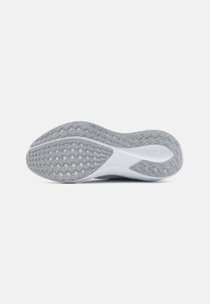 Semelle de chaussure de sport grise et blanche avec des motifs en losange pour l'adhérence, vue de dessous sur un fond uni.