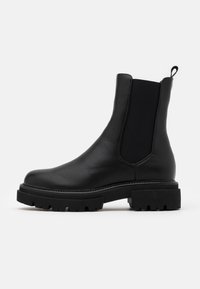 Botas Chelsea de cuero negro con paneles laterales elásticos y una lengüeta. Suelas de goma negra gruesa y texturizada con un diseño de banda de rodadura robusto.