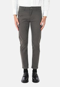 Pantaloni in cotone slim-fit verde oliva con design a cinque tasche, chiusura frontale con bottone e leggero elastico. Indossati con mocassini neri e calzini.