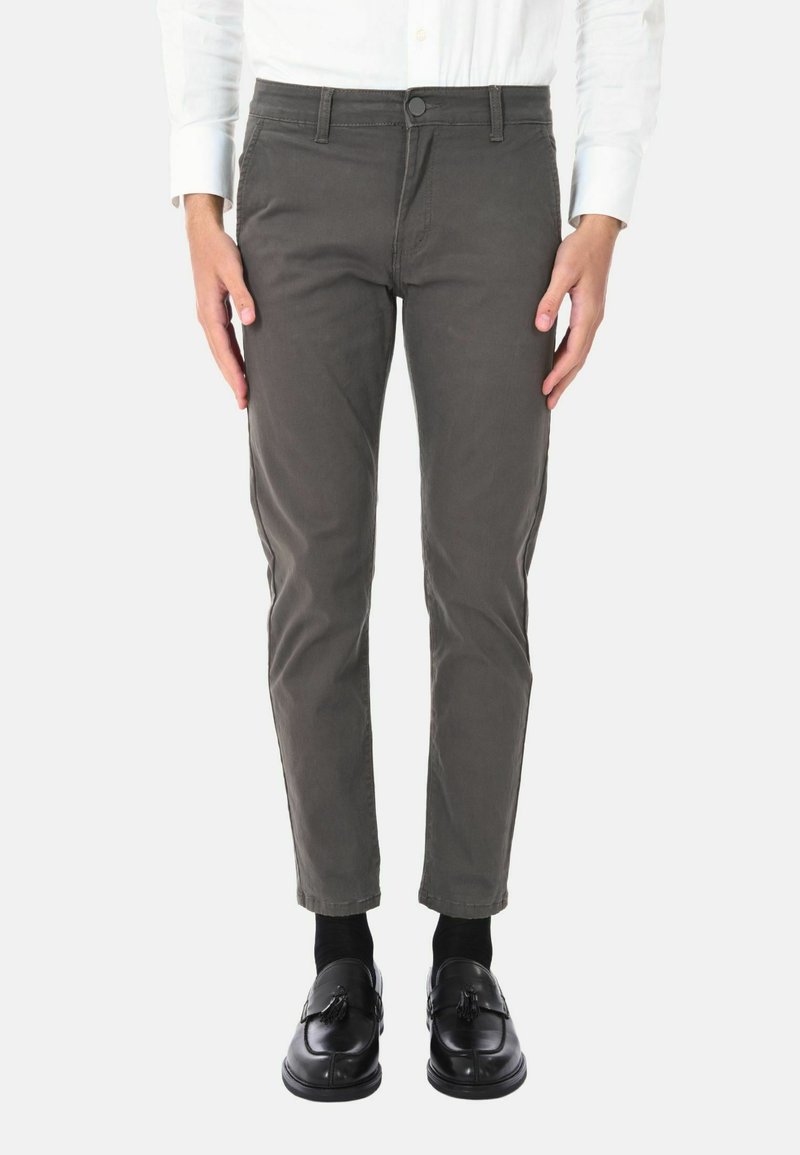 Pantaloni in cotone slim-fit verde oliva con design a cinque tasche, chiusura frontale con bottone e leggero elastico. Indossati con mocassini neri e calzini.