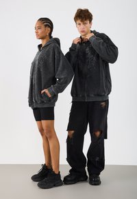 Hanorace de culoare gri închis cu accente de strasuri pe față, asortate cu blugi negri disperați și adidași negri. Design și croială casual.