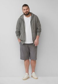 Grijze zip-up hoodie, witte t-shirt, grijze shorts en witte sneakers. Casual outfit met zachte materialen en een ontspannen pasvorm.