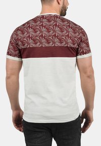 Men's t-shirt featuring a maroon patterned upper section, white lower section, short sleeves, and contrasting trim along the neckline and sleeves.