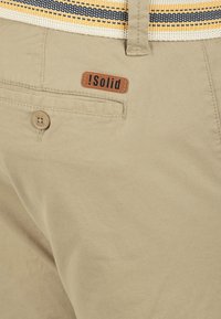 Khaki shorts lavet af struktureret stof, med en baglomme, knaplukning og et brunt lædermærke med teksten "!Solid."