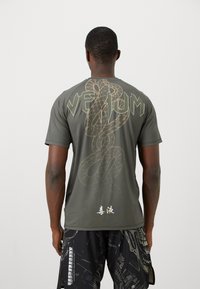 T-shirt vert foncé à manches courtes avec un grand texte "VETUM", un graphique de serpent dans une teinte plus claire et des caractères japonais en bas.