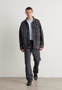 Sort denimjakke med to forlommer, lyseblå top, grå bukser og sorte sko. Rene linjer og afslappet pasform hele vejen igennem.