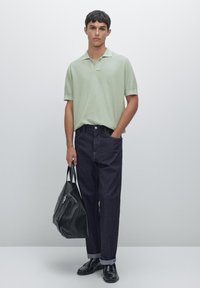 Polo shirt verde chiaro a maniche corte, jeans in denim blu scuro, borsa in pelle nera e scarpe. Design semplice con vestibilità rilassata e maniche arrotolate.