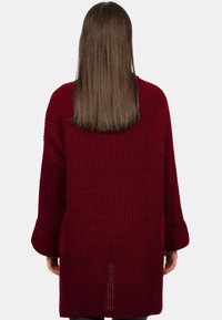 Pull en maille bordeaux à manches longues, texture côtelée, coupe oversize et fentes sur les côtés. Conçu de manière confortable, idéal pour superposer.