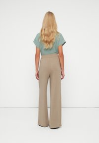 Haut vert clair à manches courtes associé à un pantalon large beige taille haute, présentant une texture lisse et une taille élastique.