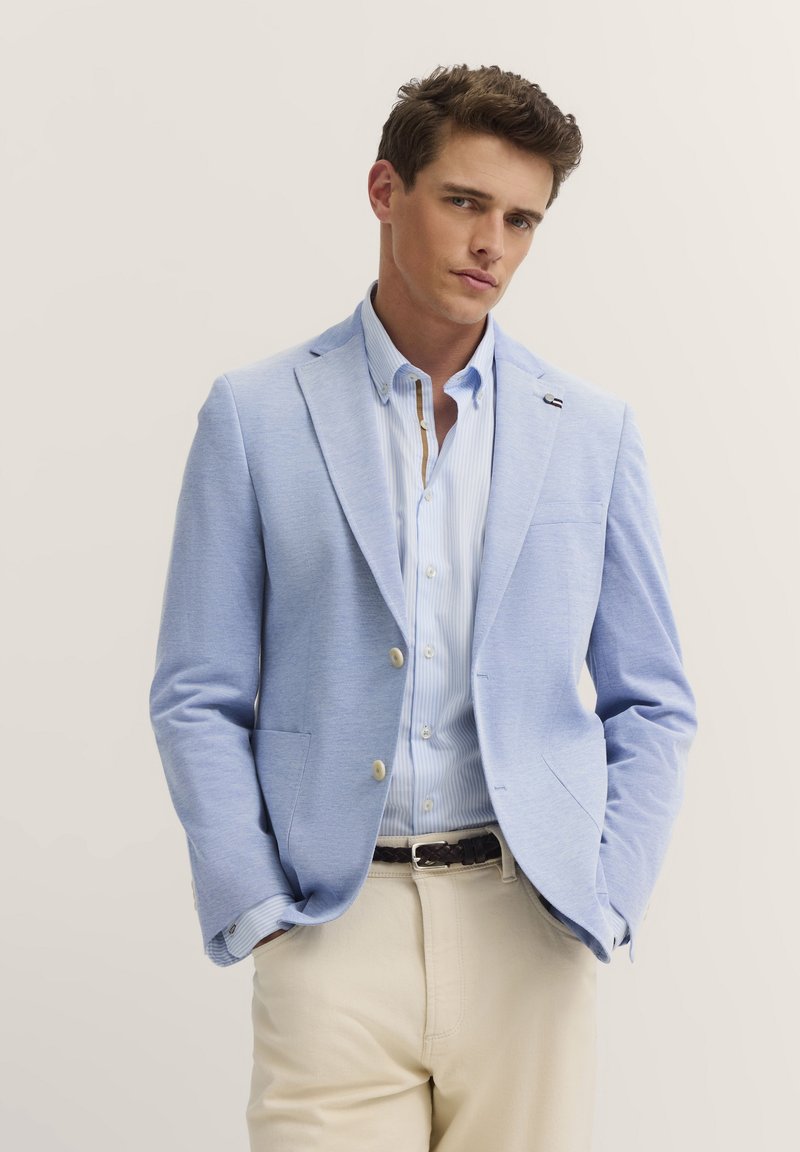 Hellblaues Blazer mit tailliertem Schnitt, leichtem Stoff, zwei Fronttaschen, kombiniert mit einem gestreiften Hemd und beigen Hosen.
