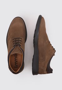 Chaussures en suede marron avec semelles en caoutchouc noir, présentant un bout rond, un laçage et une texture contrastante autour de la cheville.