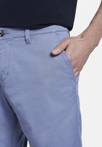 Pantaloni in cotone azzurro chiaro con vestibilità slim, dotati di tasca anteriore e chiusura con bottone in vita. Texture liscia e linee pulite.