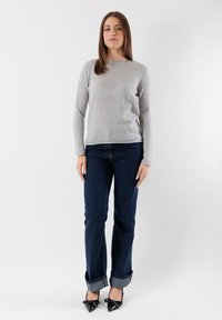 Maglione grigio chiaro lavorato a maglia, jeans blu scuro risvoltati alla caviglia e tacchi neri a punta. Design semplice con una vestibilità rilassata.