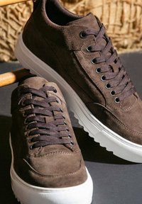 Braune Wildledersneaker mit dunkelbraunen Schnürsenkeln, runder Zehenpartie und weißer Gummisohle. Mit metallenen Ösen und subtilen Steppnähten.