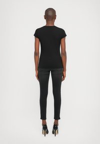 Zwarte fitted t-shirt met korte mouwen, gecombineerd met zwarte skinny jeans en zwarte hoge hakken. Glad materiaal, strakke silhouet.