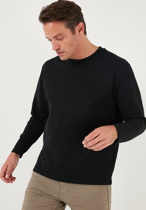 Black long-sleeve T-shirt made of cotton, featuring a crew neck and a fitted design, worn with light-colored pants. Smooth texture, no patterns.